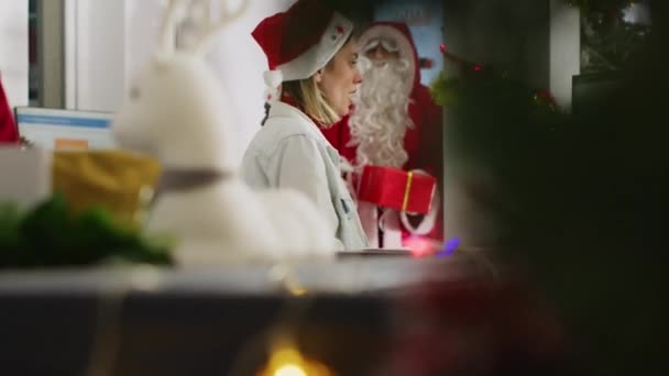 拍摄一张照片 照片中的工人们在圣诞装饰的工作场所接受同事们以圣诞老人的身份送给他们的礼物 在办公室举行的秘密圣诞晚会上 那些装模作样的同事带着礼物的令人惊讶的女人 — 图库视频影像