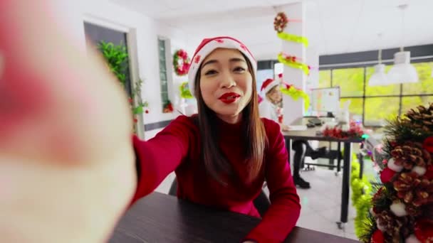 クリスマスのアジアの従業員は フロントビューカメラを使用して自分自身を撮影サンタクロースの帽子を身に着け 冬のホリデーシーズン中にオンラインビデオコール上の夫との素敵な議論を楽しんでいます — ストック動画