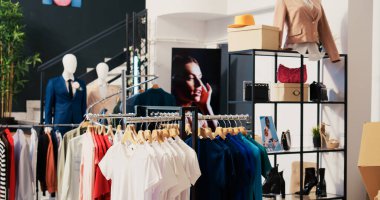 Moda mağazasında asılı günlük giyim eşyalarıyla donatılmış boş bir alışveriş merkezi. Modern butikte indirimli ürünler ve aksesuarlarla dolu raflar ve askılar. Moda konsepti