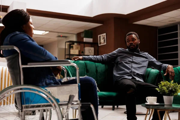Молодой Афроамериканец Разговаривает Подругой Инвалидной Коляске Сидя Вместе Вестибюле Отеля — стоковое фото