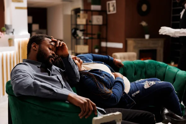 Symptoms of jet lag. African American couple arriving at destination, feeling sleepy, exhausted tourists man and woman resting sleeping on comfortable sofa in hotel lobby, waiting for check-in time