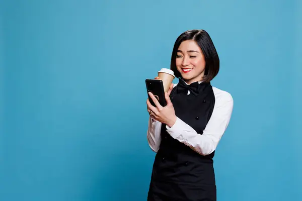 Uśmiechnięta Azjatycka Kelnerka Mundurze Kawiarni Pijąca Kawę Pisząca Smsy Smartfonie — Zdjęcie stockowe