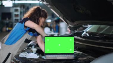 Garaj tesisinde arızalı bir arabanın üzerinde duran krom anahtarlı dizüstü bilgisayarın yakın çekim görüntüsü. Aracın içindeki mühendislik parçalarının yanındaki tamirhanede yeşil ekran cihazı.