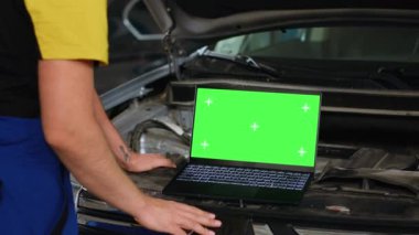 Mühendis, araba servisinde hasarlı araç için yeni parçalar sipariş etmek için yeşil ekran dizüstü bilgisayar kullanıyor. Eskilerinin yerine kullanılacak bileşenleri çevrimiçi aramak için krom anahtar aygıtı kullanan uzmanların yakın çekim görüntüsü