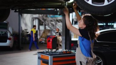 Vasıflı bir mühendis garajda araba tamirinde çalışıyor, rutin bakım sırasında lastik değiştiriyor. Araç altındaki oto tamirhanesi çalışanı potansiyel sorunları düzeltmek istiyor
