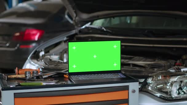 在汽车修理店关闭绿色屏幕笔记本电脑的全景截图 坐在汽车前的工作台上 旁边是专业的机械工具 车盖还在等着修理 — 图库视频影像
