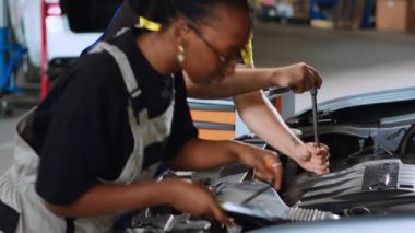 Araba servisindeki iş birliği teknisyenlerinin arızalı otomobili tamir etmek için tork anahtarı kullanarak yakın plan çekimini yap. Erkek ve Afrikalı Amerikalı kadın tamir atölyesinde profesyonel aletler kullanarak bozuk araca servis yapıyorlar.