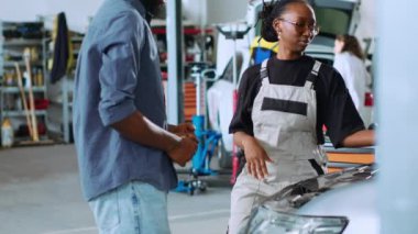 Araba tamirhanesinde müşteriye yardım eden bilgili bir tamirci. Garajda çalışan bir adam adamla araba parçalarına bakıyor, rutin kontroller sırasında aracına bakıyor.