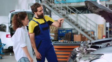 Araba servisindeki tamirci, iyileştirilmiş teknoloji hologramını kullanarak kadın otomobillerin tamir edildikten sonra otomobil tepkilerini gösteriyor. Tamirci araç motorunu test etmek için AR teknolojisini kullanıyordu