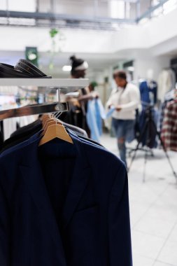 Moda butik mağazasında arka planda asılı duran resmi erkek ceketleri. Alış veriş merkezindeki askılarda ve aksesuarlarda erkek ceketleri son gelişi. Seçici odak noktasını kapat.