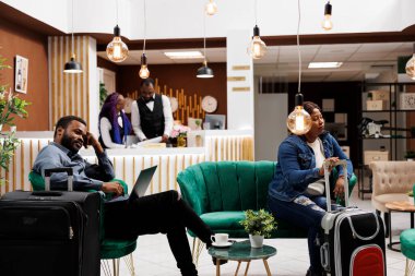Bavulu olan yorgun insanlar otel lobisinde bekliyor, Afrikalı erkek ve kadın turistler giriş yapmak için bekliyor. Siyah aile uzun bir uçuştan sonra tatil için tatil köyüne geldi.