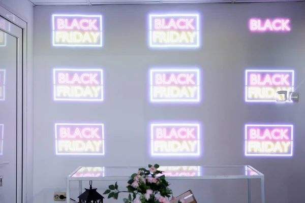 Visual displays in retail. Laser projector projecting colorful glowing neon Black Friday promotional content onto white wall to attract customers during seasonal sales, in-store marketing