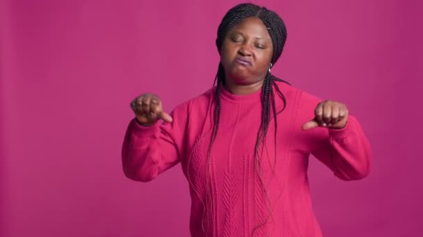 カメラに向かって親指を振るピンクのセーターでアフリカ系アメリカ人女性 大胆な孤立した背景の前に彼女の手で不承認を表示するファッションモデル — ストック動画