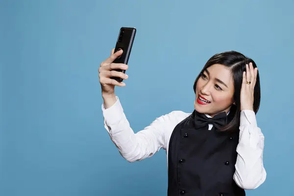 Uśmiechnięta Młoda Azjatycka Kelnerka Patrząca Przednią Kamerę Smartfona Naprawiająca Fryzurę — Zdjęcie stockowe