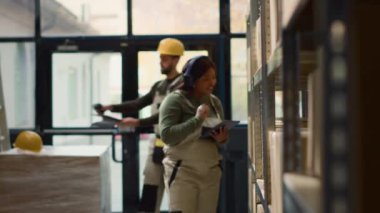 Malı incelerken müzik dinleyen lojistik şefi. Neşeli Afro-Amerikalı yönetmen depo sıralarında yürürken heafon takıyor.