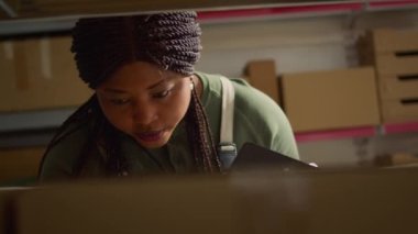 Afro-Amerikan depo işçisinin raflardaki karton kutuları tararken, paket göndermeden önce ürün etiketleri bilgilerini güncellerken yakın plan çekimleri.