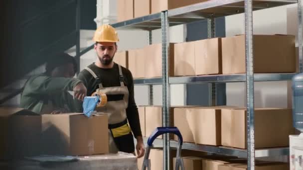 African american employee in warehouse next to coworker sealing cardboard box package ready to be shipped to customers. Workers securing packaged parcels to avoid issues during delivery process