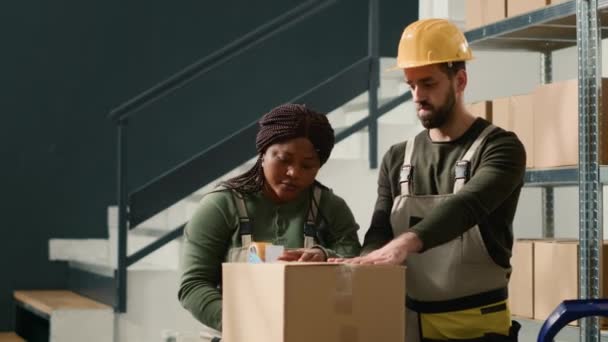 倉庫の同僚は顧客に出荷される準備ができている段ボール箱のパッケージを密封します 配達中に問題を避けるために小包を確保する貯蔵施設のスタッフ — ストック動画