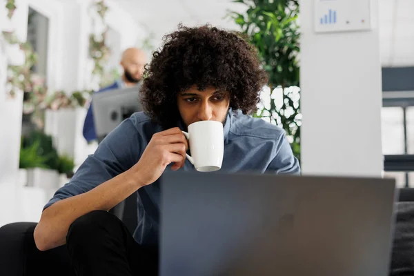 Arab start up company entrepreneur planning marketing strategy on laptop while drinking coffee. Focused young man executive manager while working overtime in business office