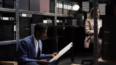 Diz üstü bilgisayarı olan Afrikalı Amerikalı dedektif ve polis kadın kanıtları inceliyor, araştırma yapıyor ve olay odasında birlikte bir dava oluşturuyorlar. Erkek polis memuru yerde otururken belgeleri inceliyor..