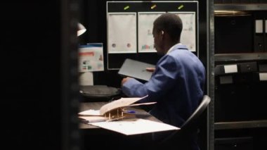 Afro-Amerikalı özel dedektif dizüstü bilgisayarını kapatıyor ve bavulunu topluyor, ofis odasından çıkıyor. Siyah polis kendi çalışma yerini kuruyor, dosyaları düzenliyor ve laptop çantasını taşıyor..