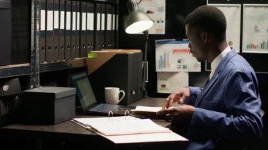 Güvenilir Afro-Amerikan müfettişi, dosyalar ve kanıtlarla çevrili, suçları çözmeye ve adaleti sağlamaya kararlı. Özel dedektif kanıtları inceliyor, gülümseyerek kameraya bakıyor..
