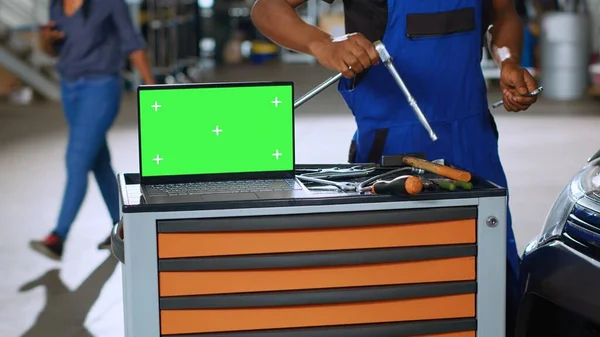 绿色屏幕笔记本电脑放在专业工具旁边繁忙车库的工作台上 修理工在模糊的背景下修理汽车 汽车修理店的彩色关键设备 — 图库照片