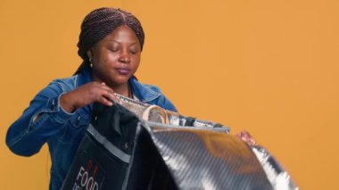 Bisikletle yemek dağıtırken, genç siyahi kadın müşteri memnuniyetini sağlamak için başparmağını kaldırıyor. Mahallede Afro-Amerikan teslimatçı çevre dostu yemek veriyor.