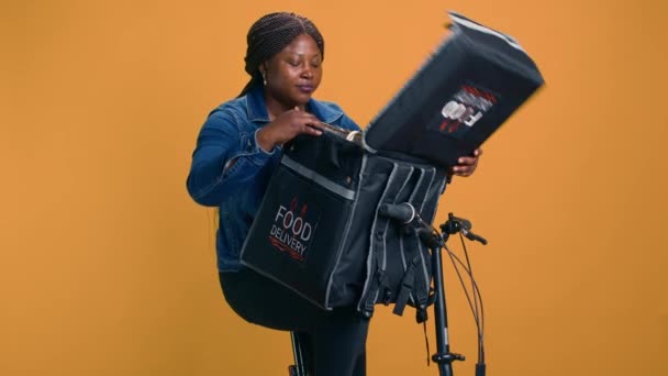 健康な若い黒人女性は 顧客満足を保証するテイクアウト食品を提供しながら親指を与えます アフリカ系アメリカ人の配達人で 近所で環境にやさしい食事の代替品を提供 — ストック動画