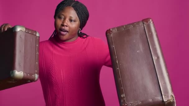 女性のアフリカ系アメリカ人旅行者は スタイリッシュな茶色のスーツケースを自信を持って展示しています ファッションで旅行する準備ができている荷物の2部分と立っている活気のある笑顔の美しい黒人女性 — ストック動画