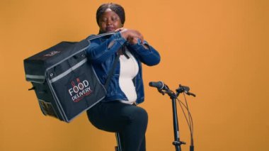 Verimli teslimatçı kadın, müşteri mahallesine bisikletle geldikten sonra fast food dağıtımı yapıyor. Afro-Amerikan kurye müşteri varış noktasında yiyecek paketini boşaltıyor..