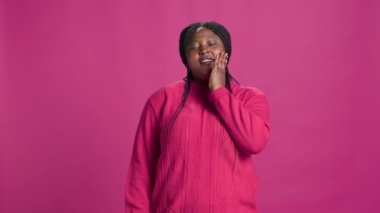 Kadın moda etkileyicisi kameranın önünde esniyor ve uzun bir günün ardından yorgunluğunu ifade ediyor. Pembe arka planda ağzı açık Afro-Amerikan modacının video görüntüleri..