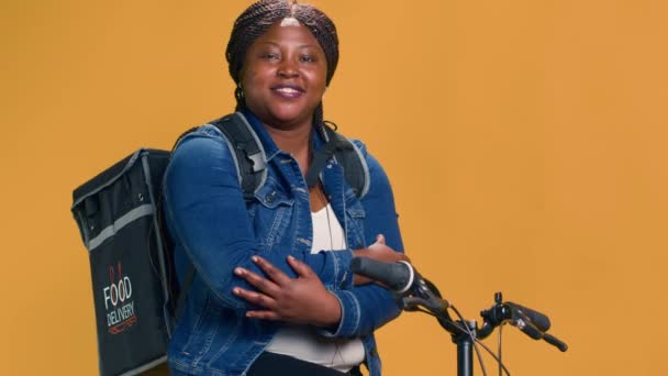 年轻的骑自行车的女骑手背着提着食物袋坐在自行车上等着送餐 非洲裔美国人自行车信使在发送包裹前休息 手持射击 — 图库视频影像