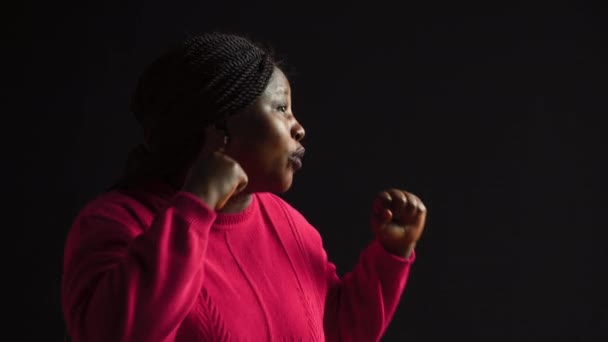 非洲裔美国妇女站在那里 双手紧握着 准备迎接挑战 年轻的女士摆出紧握着拳头的姿势 在孤立的黑色背景中表现出坚强而自信的存在 — 图库视频影像