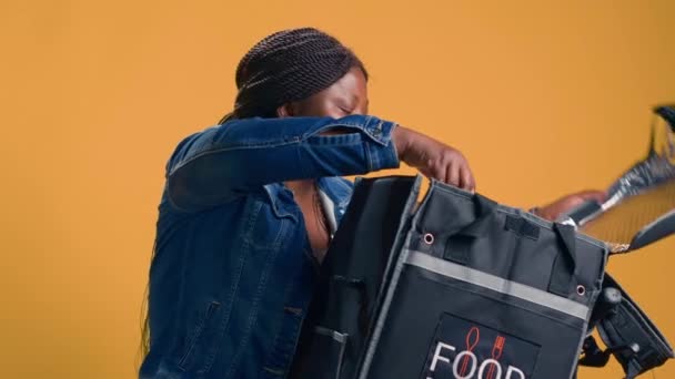 若い黒人女性宅配便は 食品配達バッグからピザ箱を取り出します 効率性は アフリカ系アメリカ人女性サイクリストが自転車で食べ物を提供するため 持続可能性を満たしています ハンドヘルドショット — ストック動画