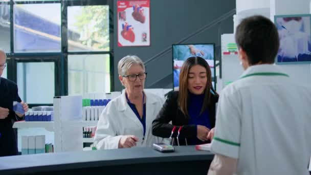 Elderly Pharmacy Assistant Helping Asian Client Pick Ideal Medicinal Products — Stock Video
