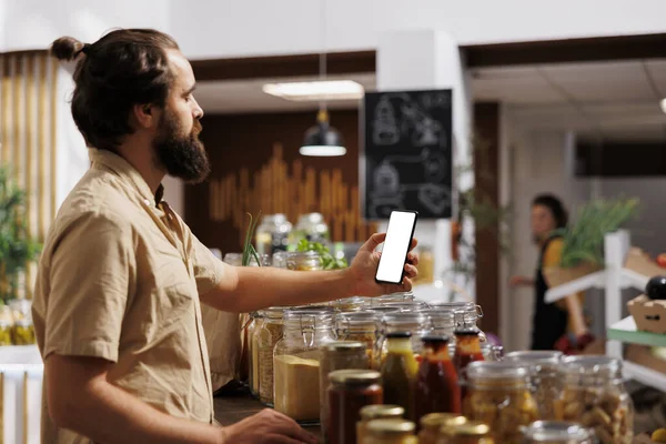 Client in zero waste shop using mockup mobile phone to videocall his wife, buying her healthy food. Customer with isolated screen smartphone phone calls partner over internet in local supermarket