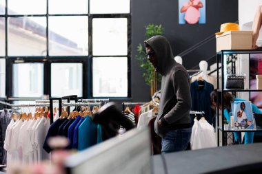 Kapüşonlu ve gözlüklü Afrikalı Amerikalı adam modern butikten şık kıyafetler çalmaya çalışıyor. Hırsız, mal çalarken birinin onu izleyip izlemediğini görmek için etrafa bakıyor.
