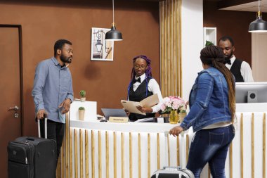Otele gelen misafirleri kayıt altına alırken Afrikalı Amerikalı kadın resepsiyon görevlileri belgeleri dolduruyor. Resepsiyonda bekleyen bayan resepsiyonist. Bavullu çift odayı bekliyor.