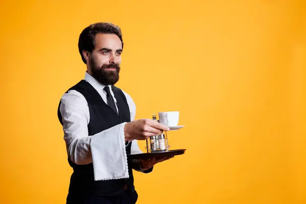 カメラでコーヒーを飲むウェイターは 立派なレストランで人々にサービスを提供するふりをしている 腕とフードプレッターの上にタオルを持っている正式な服装で熟練したスタイリッシュな男 — ストック写真