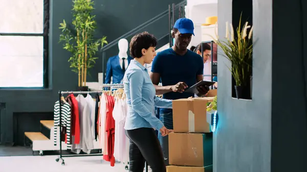 Modern butikte karton kutular taşıyan bir kuryeye yardım eden bir yönetici. Afro-Amerikan kurye, nakliye detaylarını giyim mağazasındaki işçilere açıklıyor. Moda konsepti
