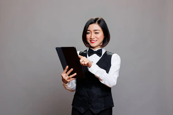 Uśmiechnięta Recepcjonistka Mundurze Sprawdzająca Listę Gości Tablecie Cyfrowym Eatery Azjatyckie — Zdjęcie stockowe