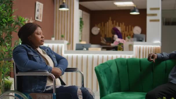 坐在轮椅上的非洲裔美国妇女与伴侣坐在休息区 在五星级酒店等待客房检查 已婚人士 长期残疾人士 旅游业 — 图库视频影像