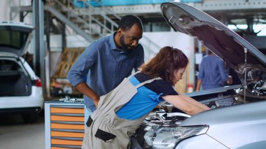 Garajdaki mühendis, müşteri izlerken motor yağı değiştirdikten sonra aracı açtı. Araba servisi çalışanı otomobili inceliyor, arta kalan sızıntıları siliyor ve müşteriyle konuşuyor.