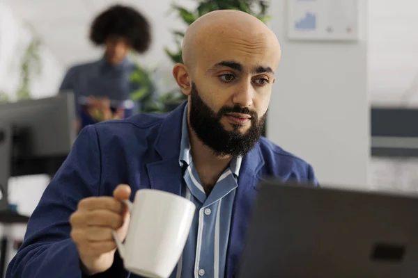 アラブのエグゼクティブマネージャーは ビジネスオフィスのノートパソコンと飲料コーヒーに関する市場調査レポートを分析します ティーカップを持ち コワーキングスペースでプロジェクトを管理する起業家 — ストック写真