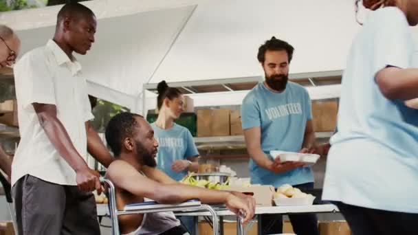 慈善组织致力于与饥饿和贫穷作斗争 向穷人提供热饭 志愿者向非洲裔美国男性轮椅使用者提供温饱食品 — 图库视频影像
