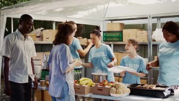 白人女孩免费打包食物 在其他慈善工作者的帮助下 分发给穷人 在室外食物库为无家可归者和饥饿者提供热饭的女性志愿者 — 图库视频影像