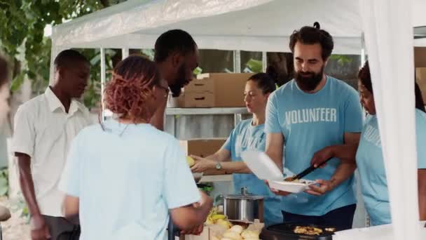 多族裔慈善组织向无家可归者和残疾人提供免费食物和食品 身穿蓝色T恤的黑人妇女帮助一个无助的 手握拐杖的非洲裔美国人 — 图库视频影像