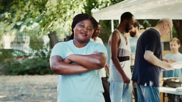 快乐的黑人女人 交叉的胳膊和蓝色的T恤看着相机 图为非洲裔美国志愿者 他们愿意帮助有需要的 贫困的和不幸的人 肖像画 三脚架拍摄 — 图库视频影像