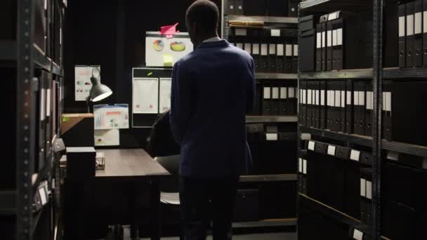 非裔美国人私家侦探拿着手提电脑袋走进档案室 开始调查犯罪 男调查员坐在办公桌前 用无线计算机检查可疑案件档案 — 图库视频影像